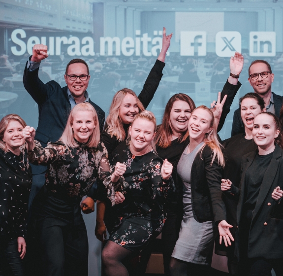 12 iloista henkilöä, jotka poseeraavat kädet ylhäällä. Kuvaa Profession ryhmätarjousta, joka kehottaa osallistumaan koulutuksiin yhdessä