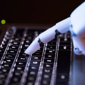 Valkoinen tekoälyn robottikäsi, joka on kirjoittamassa tietokoneella.